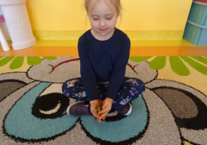Dziewczynka siedzi na dywanie, trzyma w ręku figurkę dinozaura.